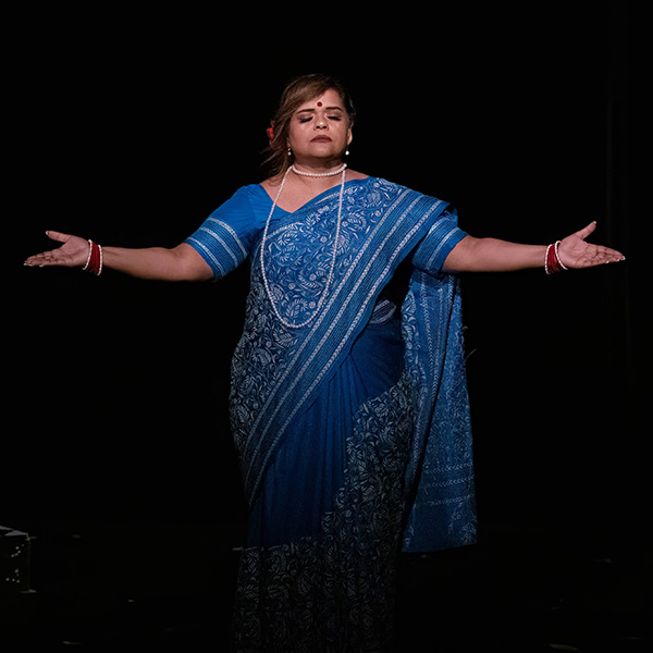 Actress in a blue sari with arms outstretched and eyes closed