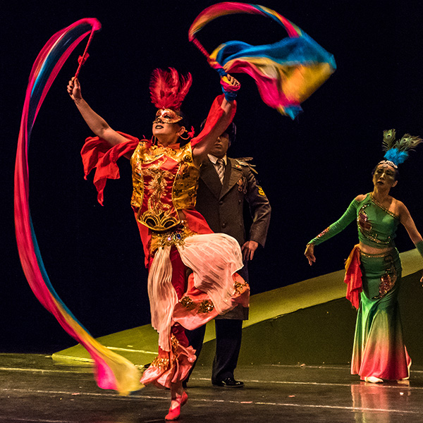 Performer dancing in mask and red costume, swirling flags on short poles