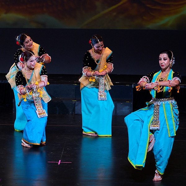 Dancers in blue costume perform on a black stage