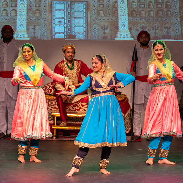Three dancers performing before a seated man wearing a crown